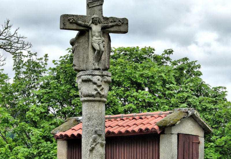 Crucero en Santo Estevo de Ribas de Sil con una calavera en el capitel y la imagen de un santo (santiño) en el fuste. Tras la imagen de Jesús crucificado se encuentra la imagen de la Virgen María.